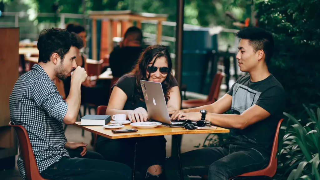 Three people gathered around a laptop at a café table