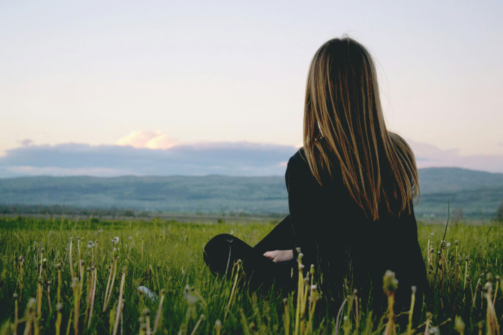 A person sitting in a grassy field, looking toward distant hills